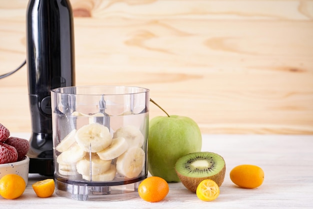 Hand blender and accessories with sliced fruit on a wooden background, space for text. Close-up.