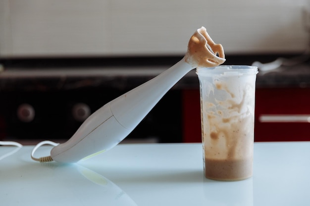 Hand blender and a shaker of Banana milkshake with the lady on background on the kitchen