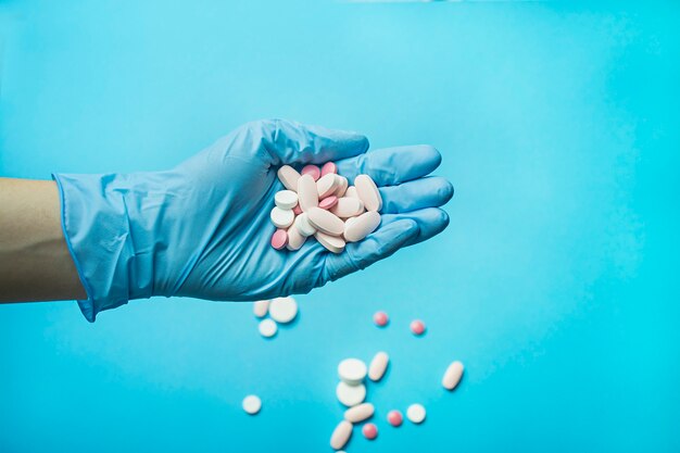 A hand in a blue glove holds pills