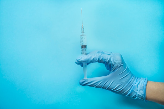 A hand in a blue glove holds a syringe. Doctor holds a syringe for vaccination. Medicine. Blue background, place for text. Copy space.