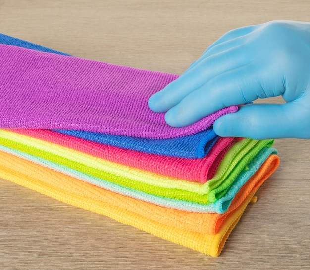 Hand in a blue glove selects a towel from a stack of bright microfiber towels for cleaning