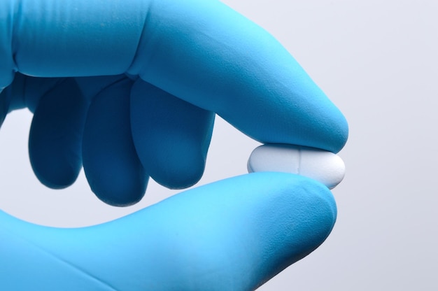 A hand in a blue medical glove holds a white pill closeup