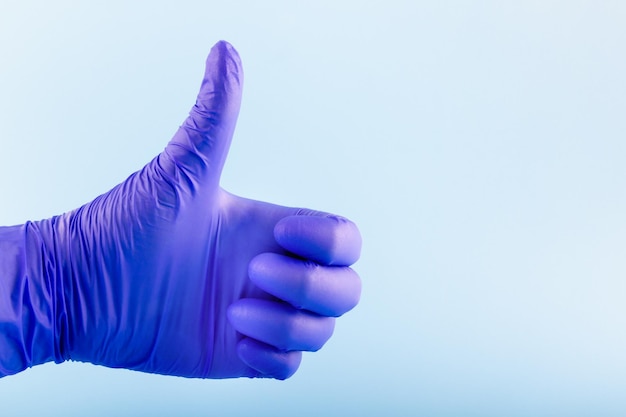 Hand in blue medical glove showing ok sign giving thumbs up\
sign protection concept