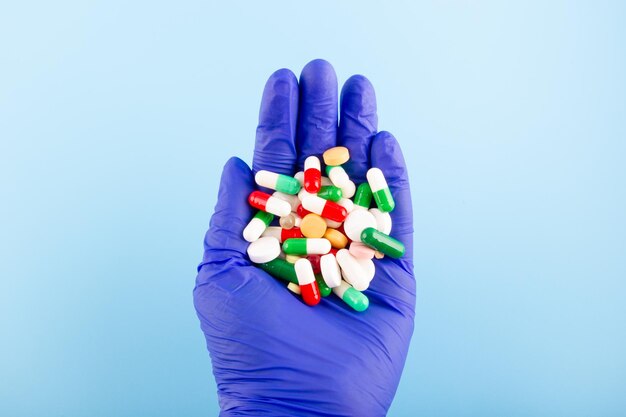 Hand in a blue medical glove with a handful of tablets and pills Medicine concept