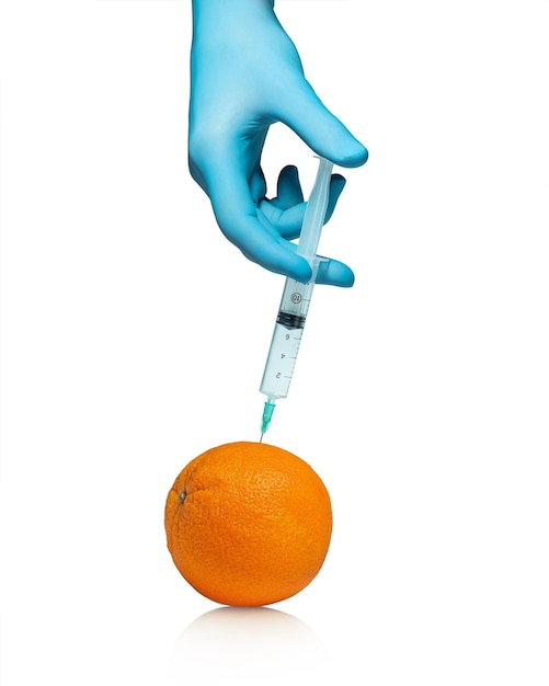 Hand in a blue medical glove with a syringe and an orange on a white background