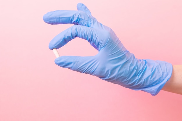 Hand in a blue medical glove with a white pill on a pink .  medicine, pharmacy, health. Minimalism, . Vertical .