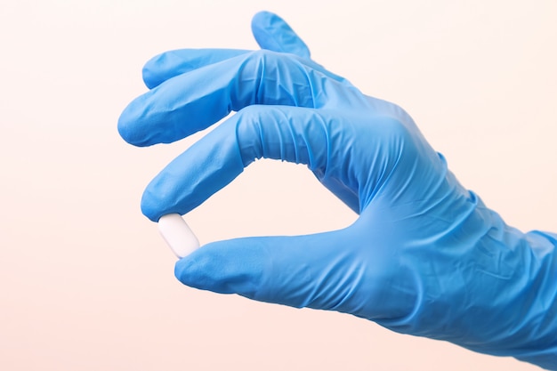 Photo hand in a blue medical glove with a white tablet on a light .  medicine, pharmacy, health. minimalism, .