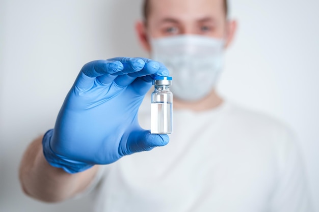 A hand in blue protective glove holding an ampoule with medicine blurred man on background