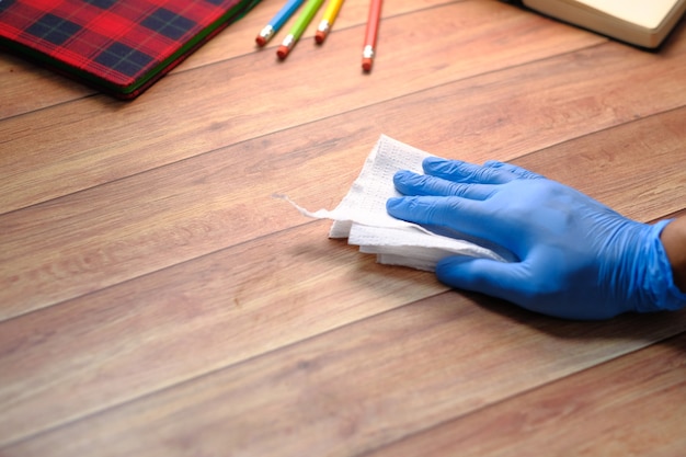 hand in blue rubber gloves cleaning table with tissue