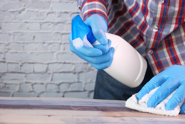 Hand in blue rubber gloves holding spray bottle and wiping flat surface