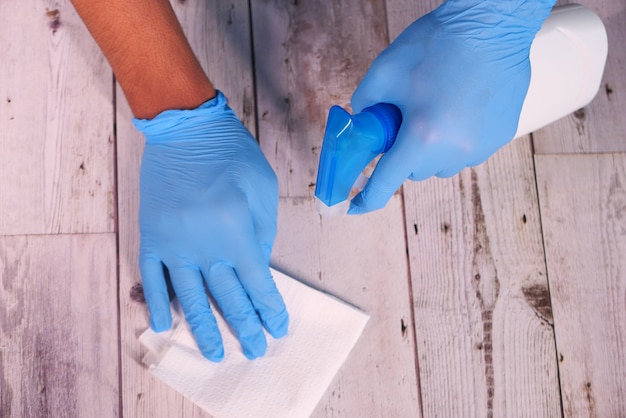 Hand in blue rubber gloves holding spray bottle and wiping flat surface