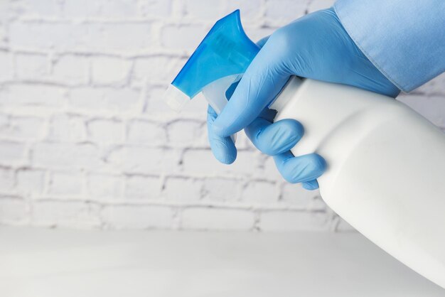 Photo hand in blue rubber gloves holding spray bottle with copy space