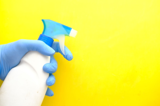Hand in blue rubber gloves holding spray bottle on yellow