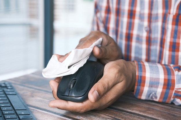 Hand in blue rubber gloves and white tissue disinfecting computer mouse