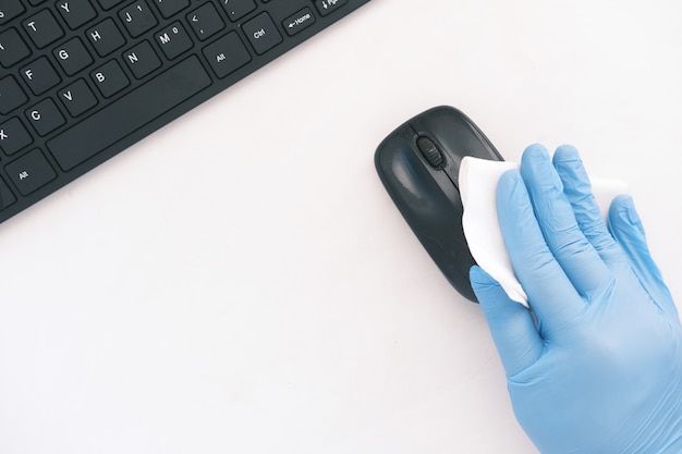 Hand in blue rubber gloves and white tissue disinfecting computer mouse