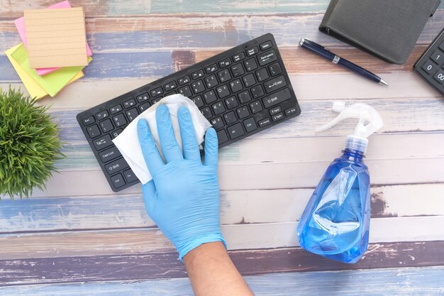 Hand in blue rubber gloves and white tissue disinfecting keyboard