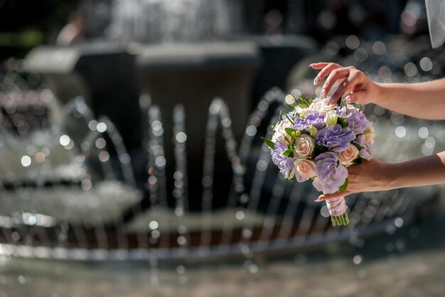 Hand of bride holding wedding bouquet on a fountain