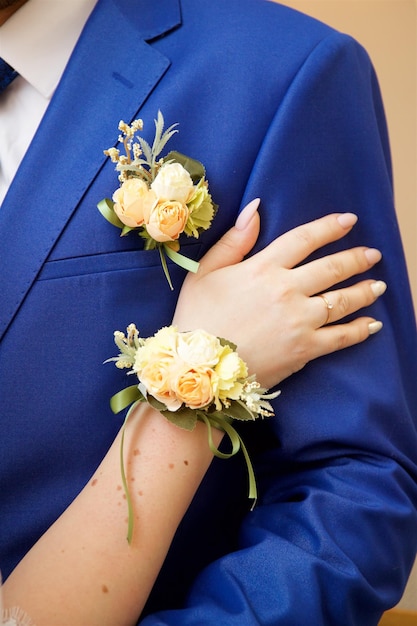 The hand of the bride with a boutonniere rests on the forearm of the groom in a blue suit with a bou