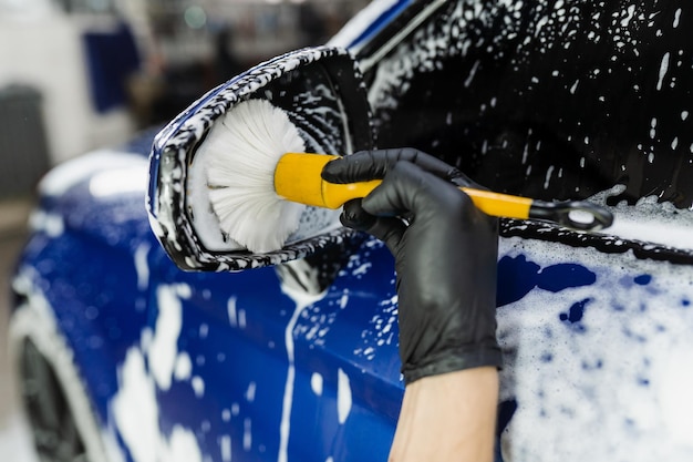 Hand brush washing of car side mirror with foam in car detailing service Car wash worker washes auto body