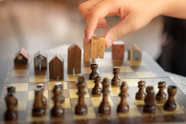 Hand of business man moving chess to Building and house models in chess game