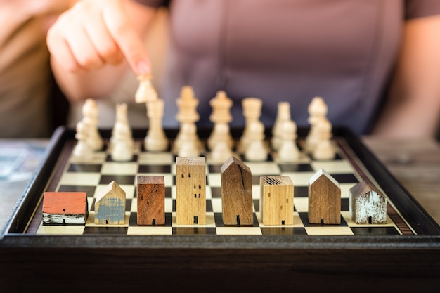 Hand of business woman moving chess to Building and house models in chess game,