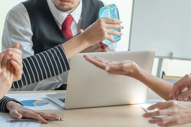 La mano della donna di affari schiaccia il gel dell'alcool del disinfettante al collega nel luogo di lavoro di riunione