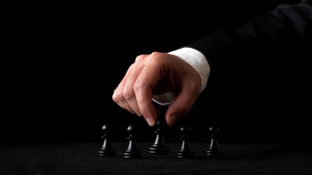 Hand of a businessman arranging chess figures in a conceptual image of leadership and power. Over black background.