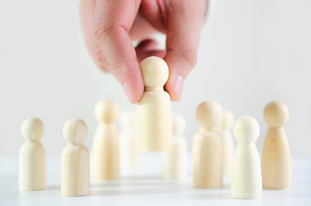 Hand of a businessman choosing wooden figure in conceptual image of search, hiring, business tactics and strategy, management.