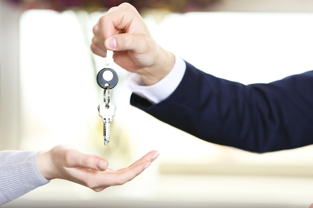 Hand of businessman giving keys to female hand on blurred background