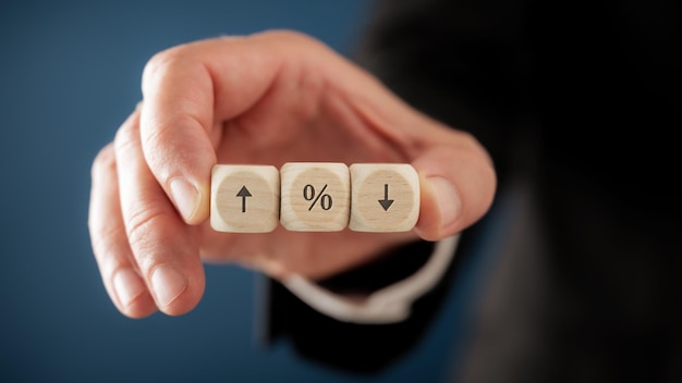 Hand of a businessman holding wooden dice with percent symbol and arrows pointing up and down