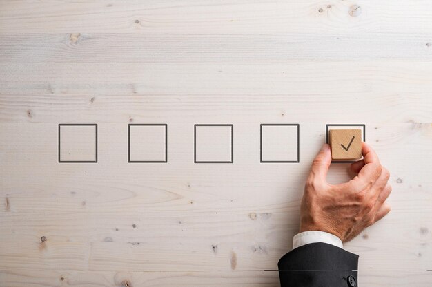 Hand of a businessman placing wooden block with a check mark on it in a last check box in the line of five