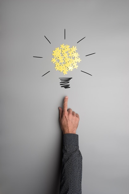 Hand of a businessman pointing on a light bulb made of yellow puzzle pieces