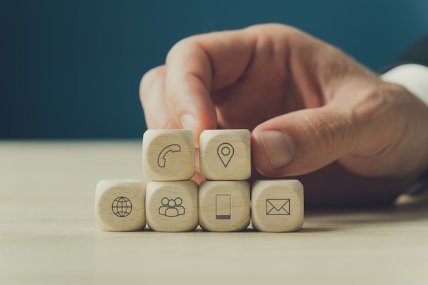 Hand of a businessman stacking wooden dices with contact and information icons on them