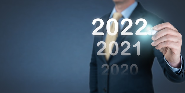 仮想画面に2022年の番号を書く手のビジネスマン。ビジネスとテクノロジーの目標は、2022年の新年の決議、計画、および立ち上げ戦略とアイデアで目標と達成を設定しました