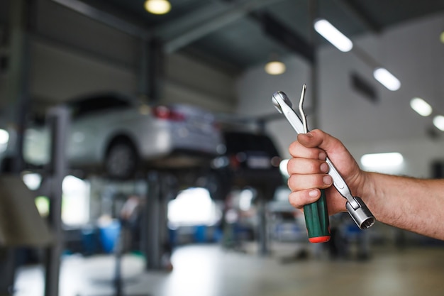 The hand of a car repairman with special tool on the service area.