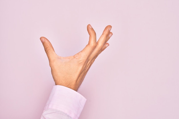 Hand of caucasian young man showing fingers over isolated pink background picking and taking invisible thing holding object with fingers showing space