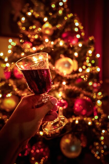 Foto mani che applaudono con un bicchiere di vino rosso inclinato contro luci di albero di natale sfocate xmas festivo