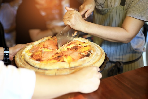 Hand chefs with knife slice Hot homemade pizza with melting lava cheese.