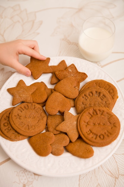 A hand of a child taking freshly made home holiday cookies in shapes of starts hearts and circles