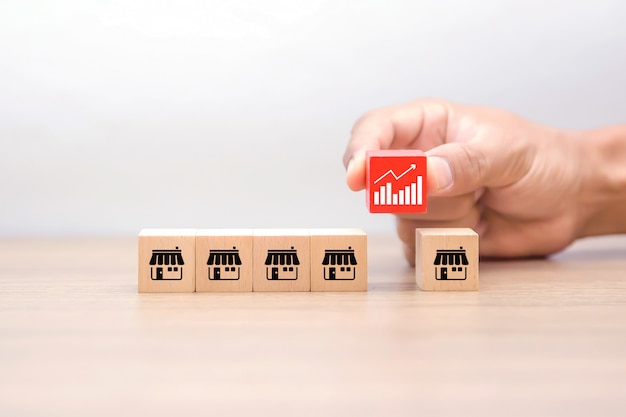 Hand chooes a cube shape wooden toy blog with business graph symbol and franchise marketing icons.