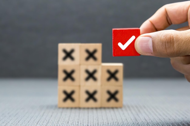 Hand choose check mark on cube wooden toy block with cross symbol for true or false changing mindset or way of adapting to change leader and transform quiz answer and poll concept