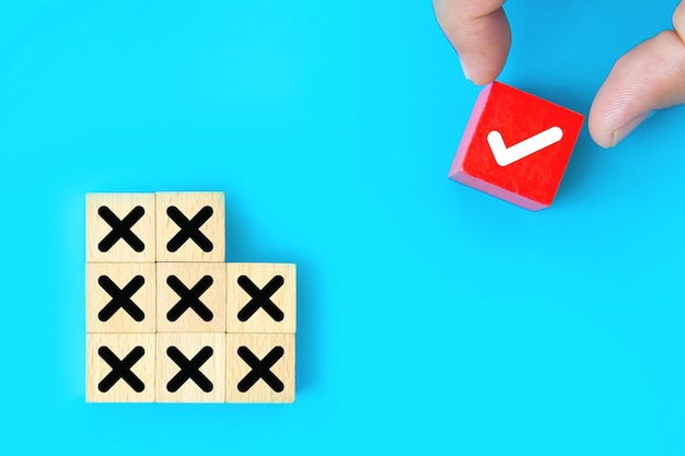 Hand choose check mark on cube wooden toy block with cross symbol