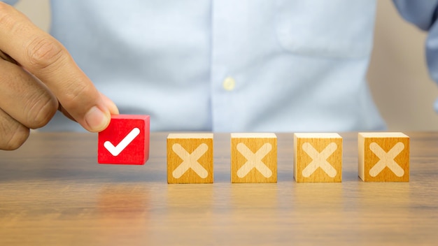 Photo hand choose check mark on cube wooden toy block with cross symbol