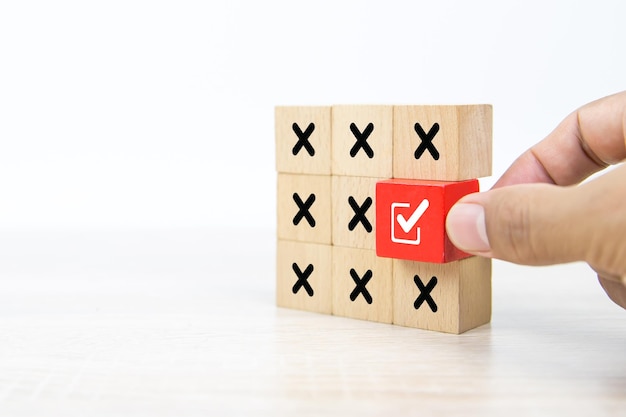 Hand choose check mark on wooden block stacked with cross symbol
