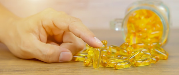 Hand choose cod liver oil capsule on the table.