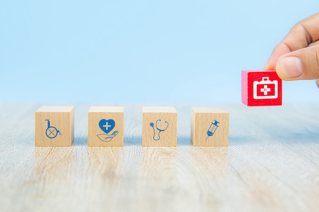 Foto la mano sceglie il blocchetto di giocattolo di legno del cubo con l'icona della borsa dell'attrezzatura medica