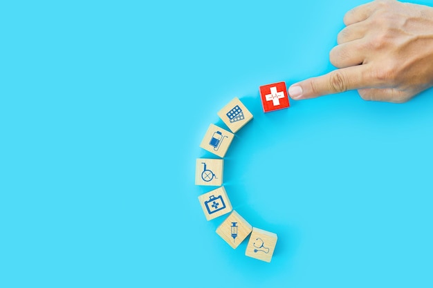 La mano sceglie il cubo di blocchi di giocattoli in legno impilati con il segno della croce rossa su altre icone di assistenza sanitaria