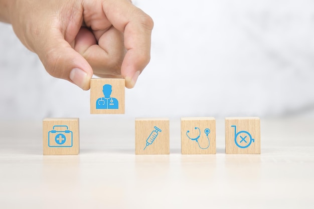 Hand choose doctor icon on cube wooden block stack with health care and medical symbol concept of healthy or sick prevent and safety insurance planner