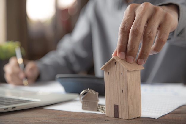 Scegli a mano una casa in legno con le chiavi di casa sulla scrivania con documenti di prestito bancario