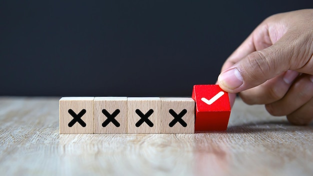 Hand chooses check mark on wooden toy with cross symbol